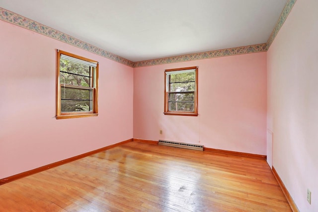 empty room with a healthy amount of sunlight, a baseboard radiator, and light wood-type flooring