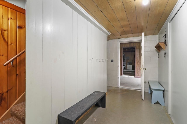 hallway featuring wooden ceiling, wooden walls, and concrete floors