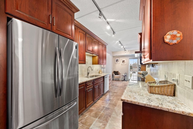 kitchen featuring stainless steel appliances, tasteful backsplash, a sink, a textured ceiling, and light stone countertops