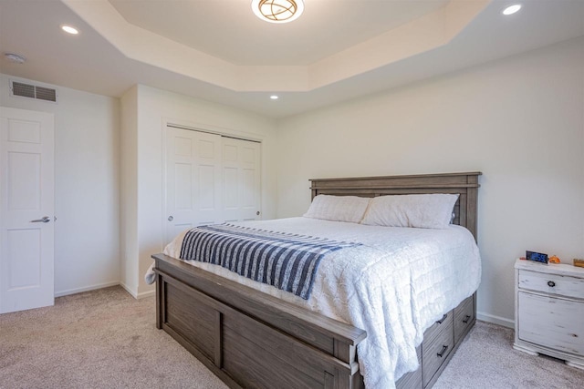 carpeted bedroom with a raised ceiling and a closet