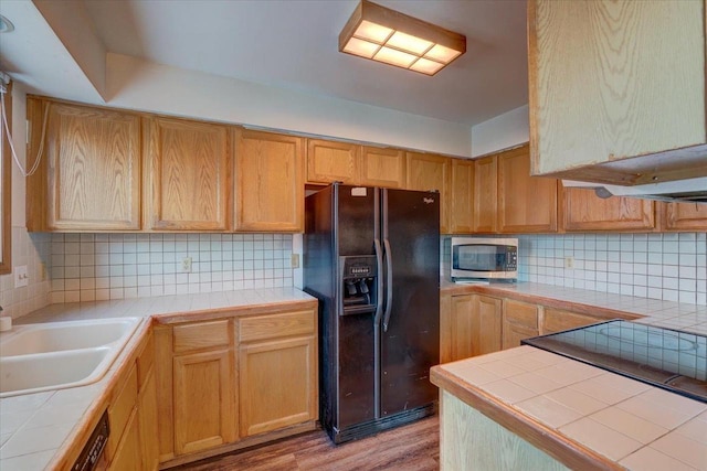 kitchen featuring tile countertops, black fridge, light hardwood / wood-style flooring, and decorative backsplash