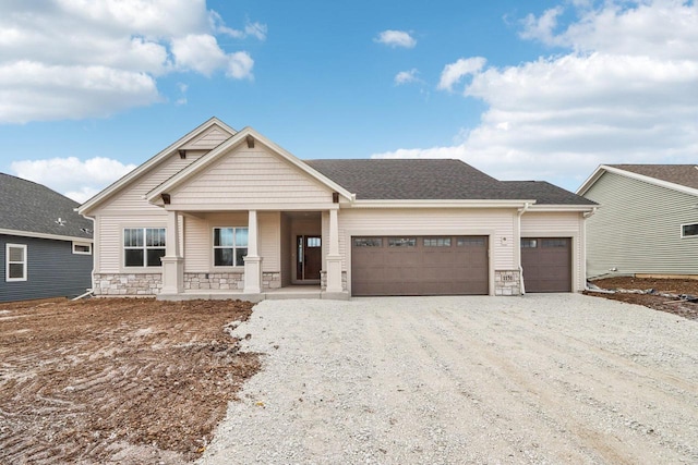 craftsman-style home featuring a shingled roof, a porch, a garage, stone siding, and driveway