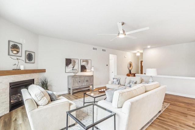 living room featuring light wood-style floors, visible vents, and a stone fireplace