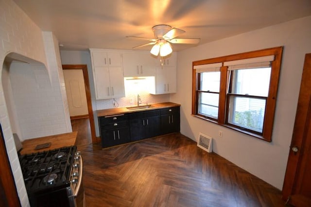 kitchen featuring dark parquet flooring, white cabinets, black gas stove, sink, and ceiling fan