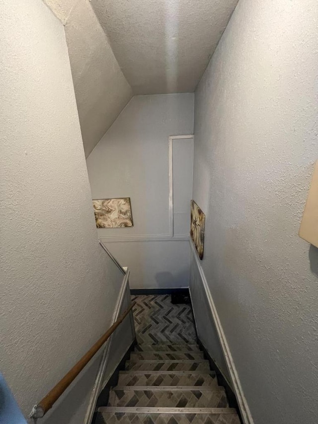 stairway with lofted ceiling and a textured ceiling