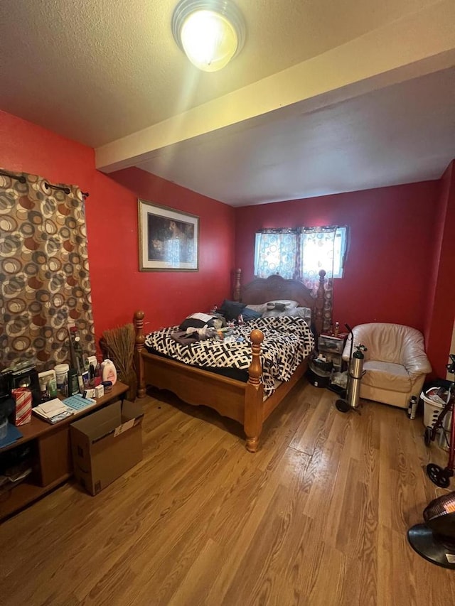 bedroom featuring beamed ceiling, wood-type flooring, and a textured ceiling