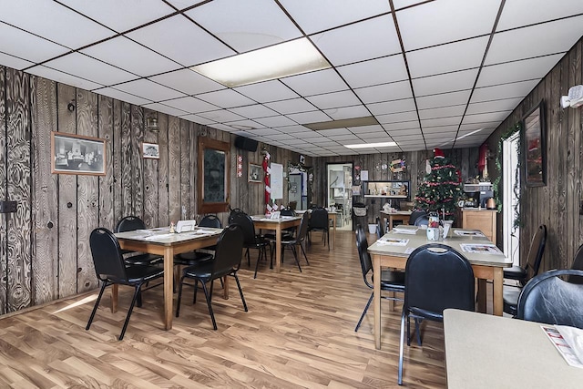 dining room with hardwood / wood-style flooring, a drop ceiling, and wood walls