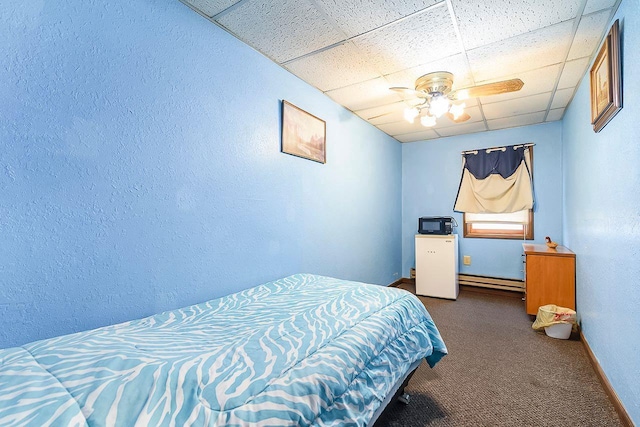 bedroom featuring baseboard heating, a paneled ceiling, ceiling fan, and dark colored carpet