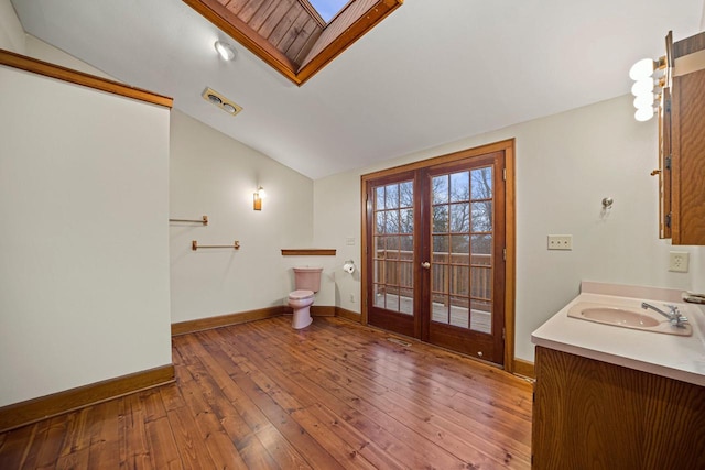 bathroom with vaulted ceiling with skylight, vanity, wood-type flooring, and french doors