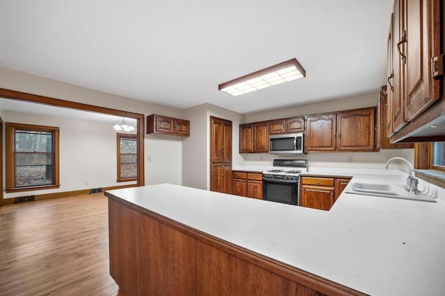 kitchen featuring kitchen peninsula, stove, light wood-type flooring, sink, and an inviting chandelier