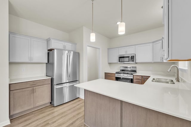 kitchen featuring sink, light hardwood / wood-style flooring, appliances with stainless steel finishes, decorative light fixtures, and kitchen peninsula