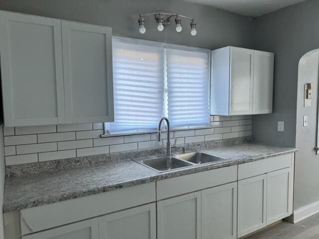 kitchen with decorative backsplash, sink, white cabinets, and light wood-type flooring