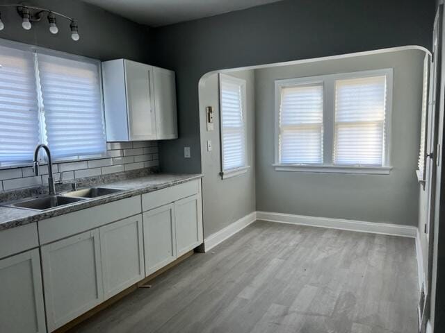 kitchen featuring backsplash, white cabinetry, sink, and light hardwood / wood-style flooring