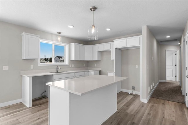 kitchen with sink, white cabinetry, hanging light fixtures, light wood-type flooring, and a kitchen island