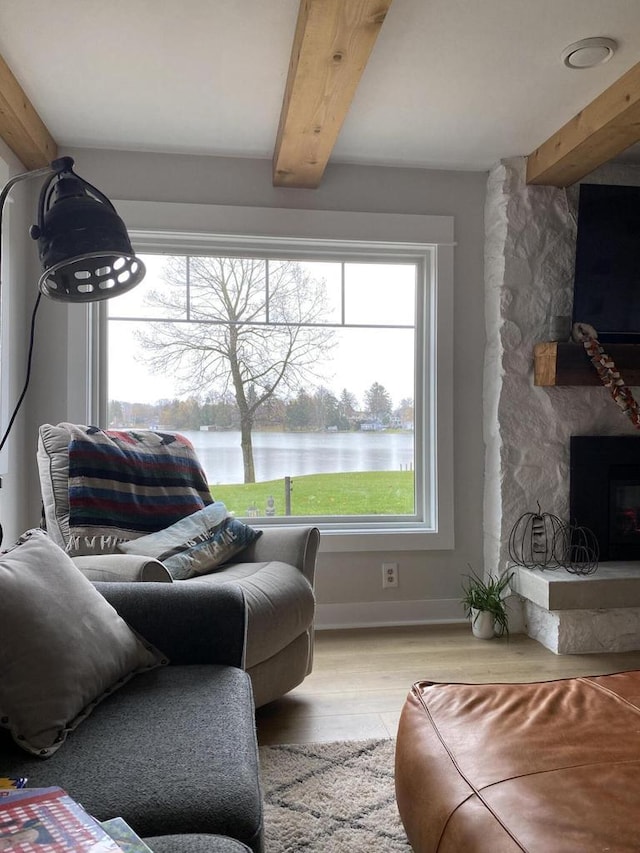 living room featuring beam ceiling, a water view, light wood-type flooring, and a fireplace