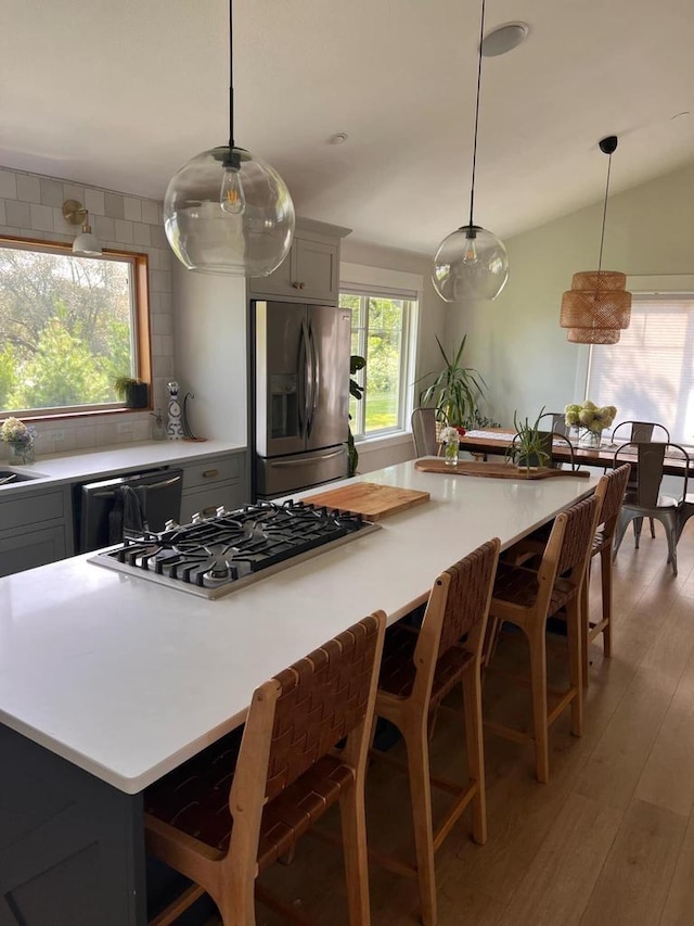 kitchen with a kitchen bar, decorative light fixtures, stainless steel appliances, and gray cabinets