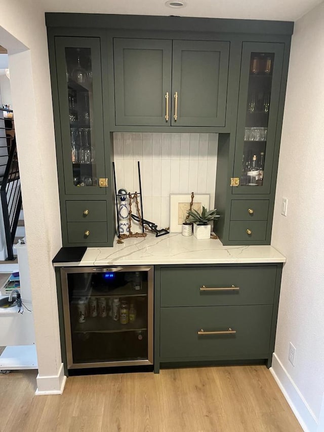 bar with tasteful backsplash, wine cooler, light stone counters, light hardwood / wood-style flooring, and green cabinets