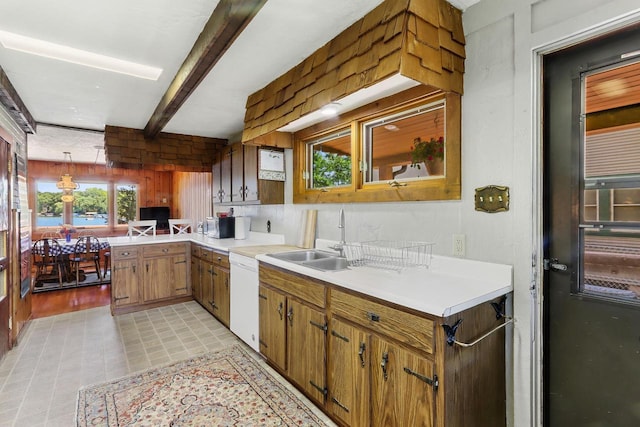 kitchen with kitchen peninsula, white dishwasher, sink, beam ceiling, and pendant lighting