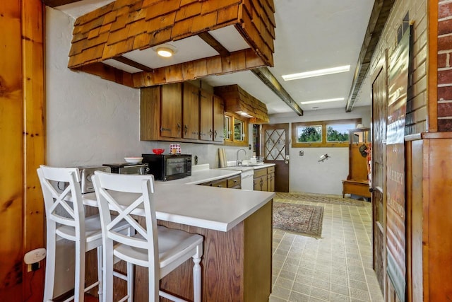 kitchen featuring white dishwasher, a kitchen breakfast bar, sink, beamed ceiling, and kitchen peninsula