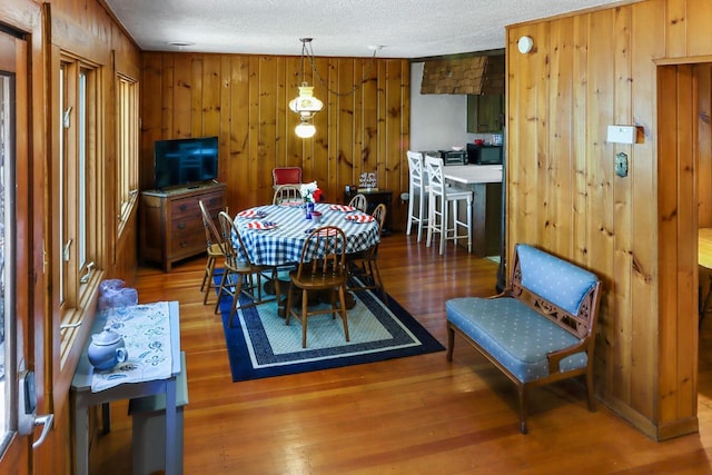 dining room with wooden walls, wood-type flooring, and a textured ceiling