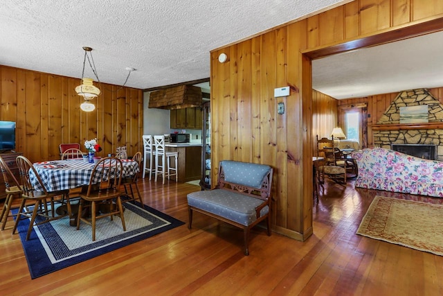 dining area with wood walls, a fireplace, dark wood-type flooring, and a textured ceiling