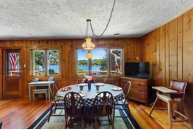 dining area featuring wood walls, wood-type flooring, and a textured ceiling