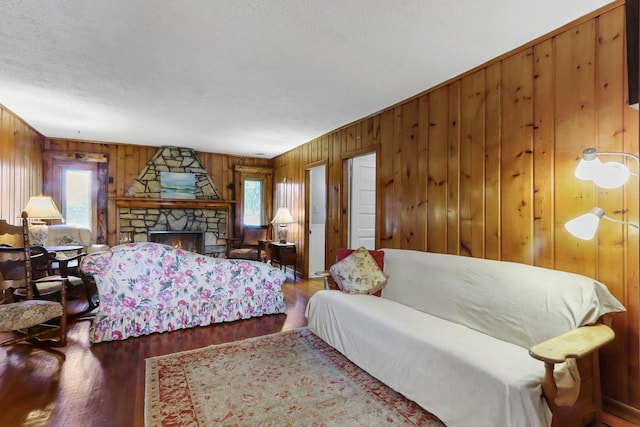 bedroom featuring hardwood / wood-style flooring, a stone fireplace, a textured ceiling, and wooden walls