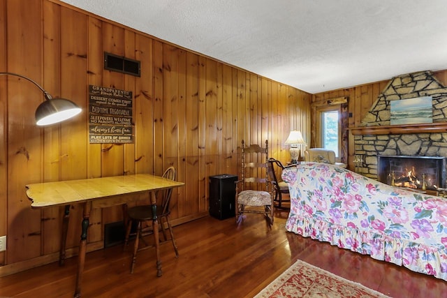 bedroom with a fireplace, a textured ceiling, dark hardwood / wood-style floors, and wood walls