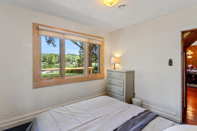 bedroom featuring wood-type flooring, a textured ceiling, and a water view