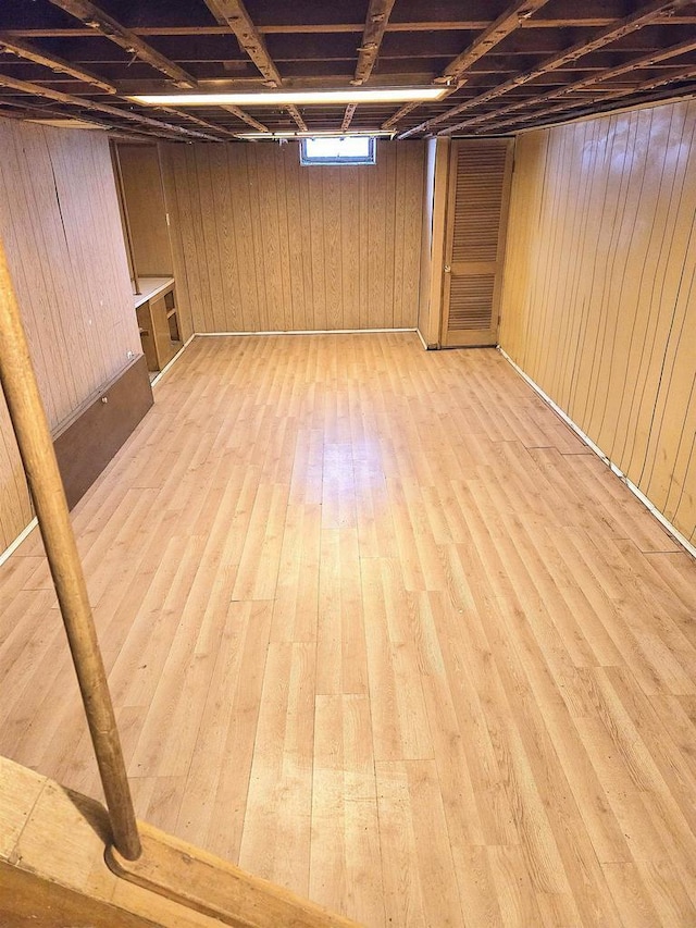 basement featuring light wood-type flooring and wood walls