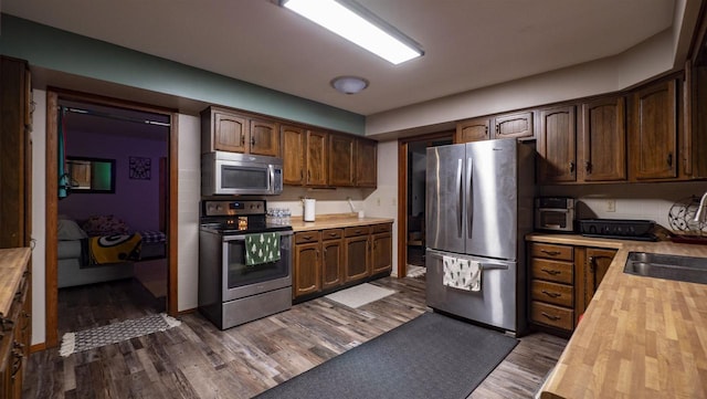 kitchen featuring sink, stainless steel appliances, dark hardwood / wood-style flooring, wooden counters, and dark brown cabinets