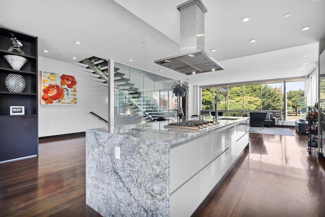 kitchen with a large island, dark hardwood / wood-style flooring, island exhaust hood, stainless steel gas stovetop, and white cabinets