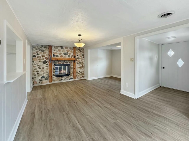 unfurnished living room featuring wood-type flooring, a textured ceiling, and a stone fireplace