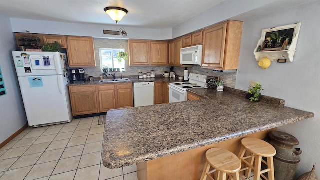 kitchen featuring kitchen peninsula, white appliances, sink, a breakfast bar area, and light tile patterned flooring