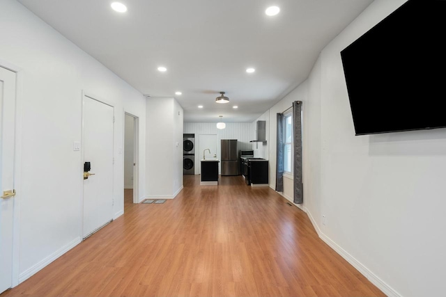 unfurnished living room with sink, light hardwood / wood-style flooring, and stacked washer and clothes dryer