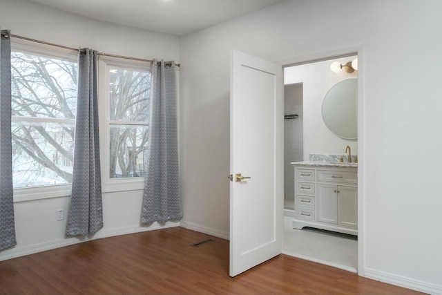 unfurnished bedroom featuring ensuite bathroom, hardwood / wood-style flooring, multiple windows, and sink