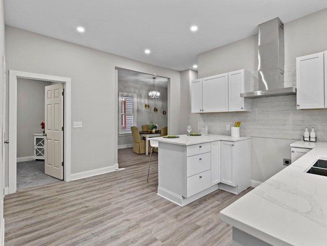 kitchen featuring white cabinetry, wall chimney exhaust hood, backsplash, kitchen peninsula, and light wood-type flooring