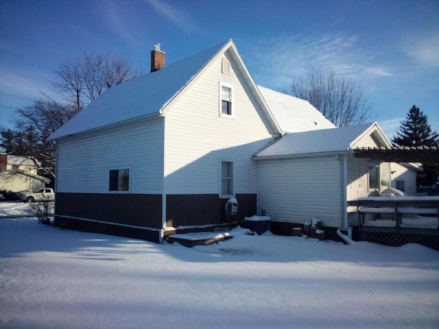 snow covered rear of property featuring a chimney