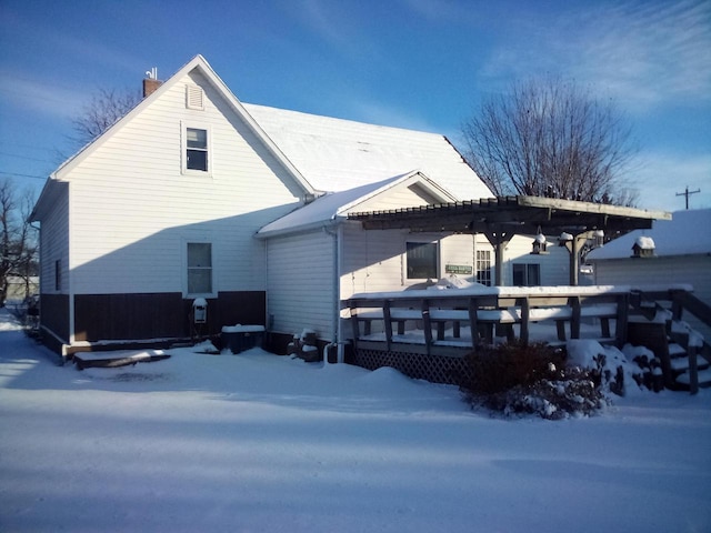 snow covered property featuring a wooden deck, a chimney, and a pergola