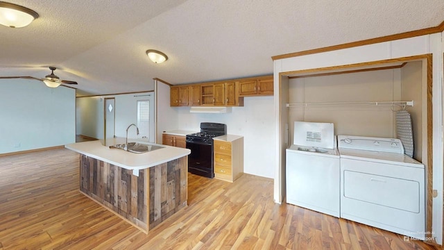 kitchen featuring a textured ceiling, black gas range oven, washing machine and clothes dryer, sink, and light hardwood / wood-style flooring