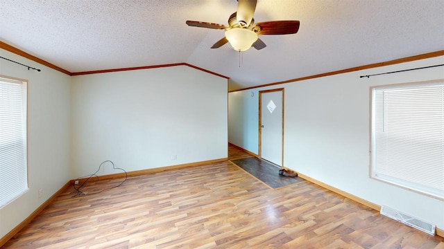 empty room with light hardwood / wood-style floors, ceiling fan, vaulted ceiling, a textured ceiling, and crown molding