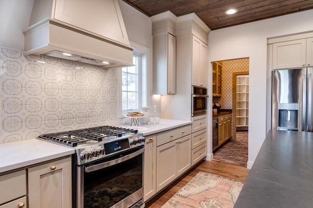 kitchen with white cabinetry, tasteful backsplash, wood-type flooring, appliances with stainless steel finishes, and custom range hood