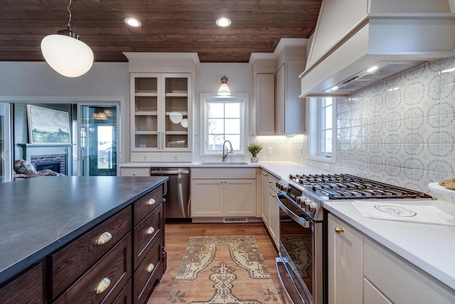 kitchen featuring sink, stainless steel appliances, custom range hood, white cabinets, and decorative light fixtures