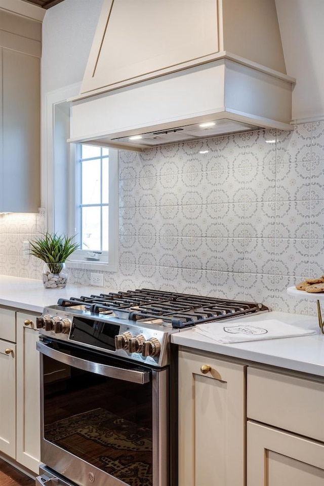 kitchen with backsplash, stainless steel range with gas cooktop, custom range hood, and white cabinets