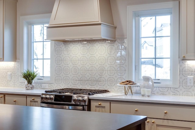 kitchen featuring backsplash, custom exhaust hood, stainless steel range with gas stovetop, and white cabinets