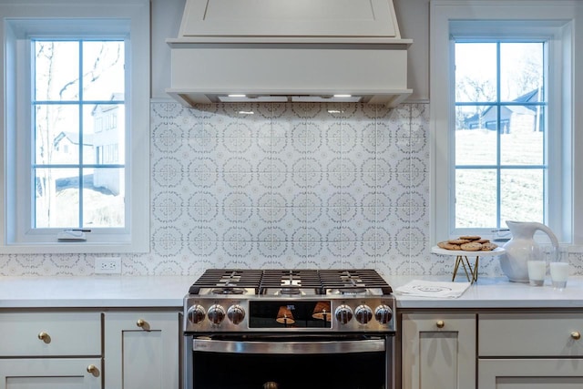 kitchen with stainless steel gas stove, backsplash, white cabinetry, and custom exhaust hood