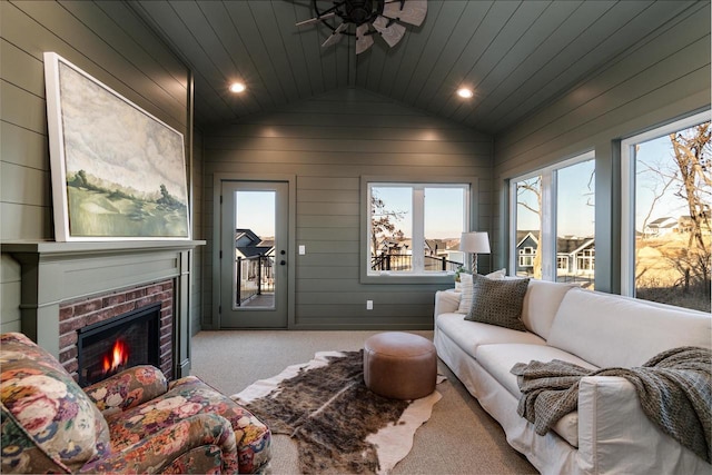 carpeted living room with ceiling fan, wooden walls, a brick fireplace, vaulted ceiling, and wooden ceiling