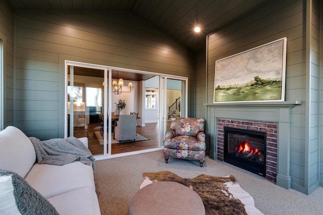 carpeted living room featuring lofted ceiling, a fireplace, an inviting chandelier, and wood walls