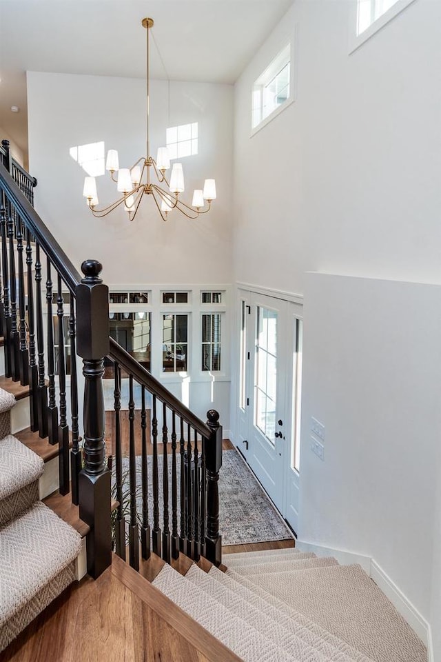 stairway with wood-type flooring, a towering ceiling, a notable chandelier, and french doors