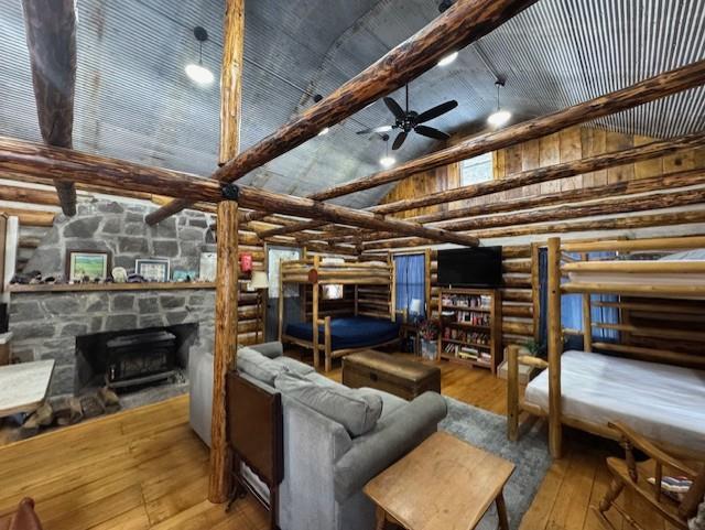 living room with high vaulted ceiling, ceiling fan, a fireplace, log walls, and light hardwood / wood-style floors